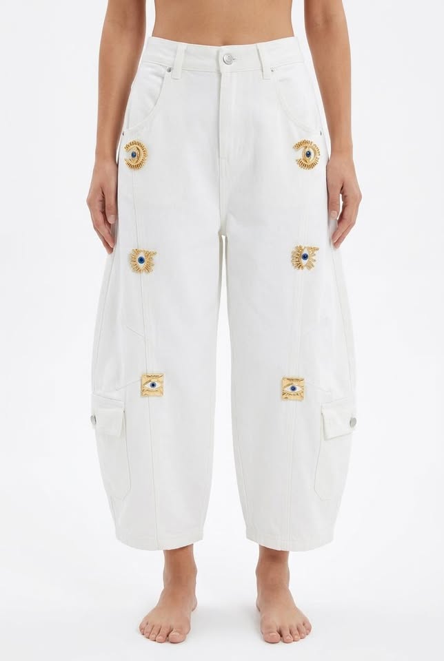 White wide-leg cropped cargo jeans with eye motifs and heavy-duty metal buckles, worn with a bare midriff.