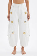 White wide-leg cropped cargo jeans with eye motifs and heavy-duty metal buckles, worn with a bare midriff.