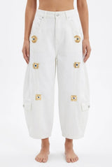 White wide-leg cropped cargo jeans with eye motifs and heavy-duty metal buckles, worn with a bare midriff.